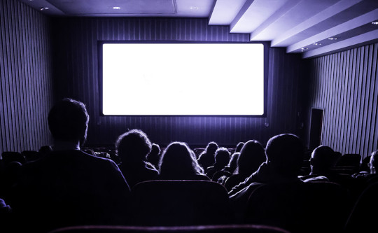 зритель в темноте кинозала смотрит на экран